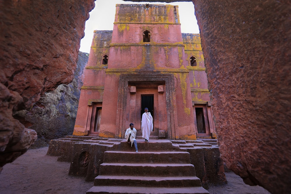 person in white dress in front of pink building