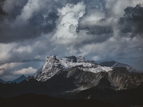 A dramatic drone shot of a mountain ridge under a cloudy sky.