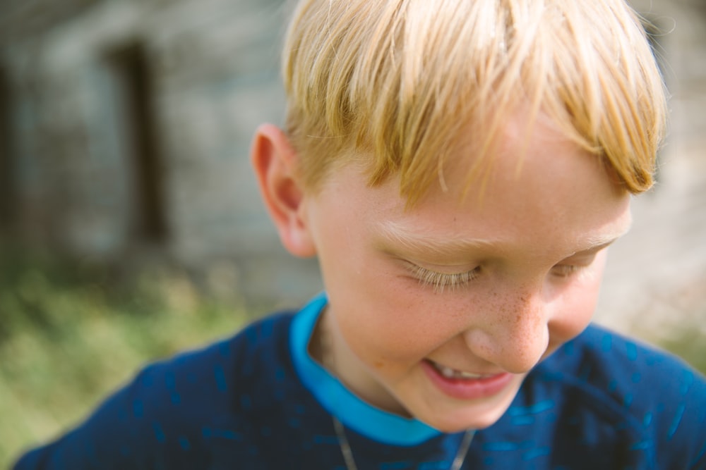 selective focus photography of boy in blue shirt looking down near house