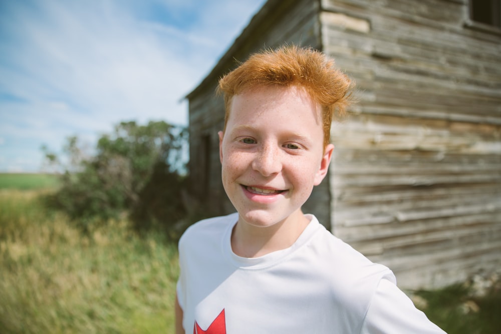 selective focus photography of smiling boy in white and red crew-neck shirt near house