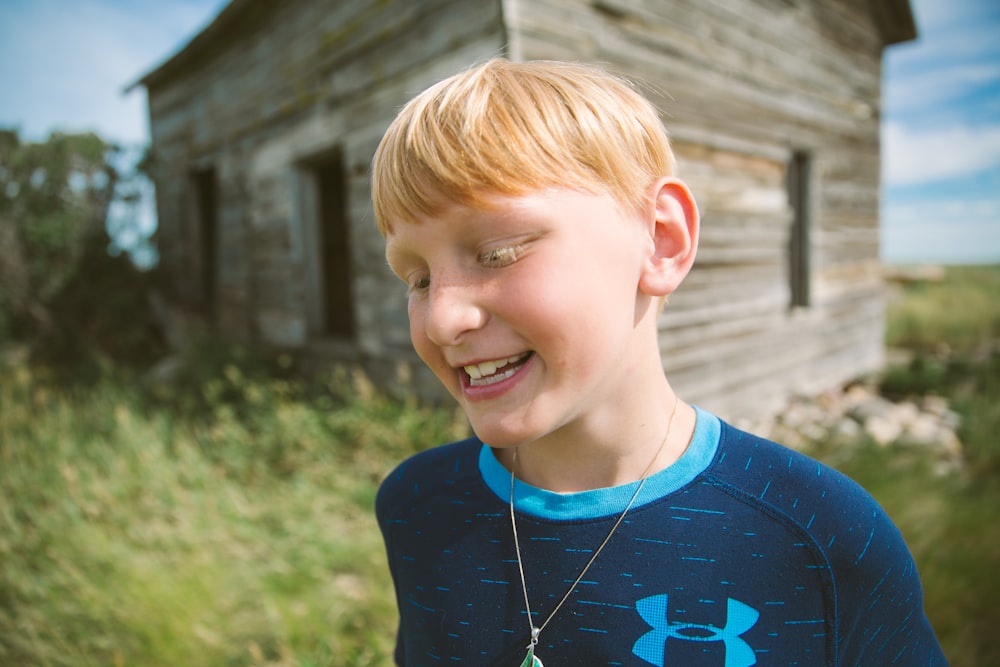selective focus photography of boy in Under Armour shirt beside wooden house