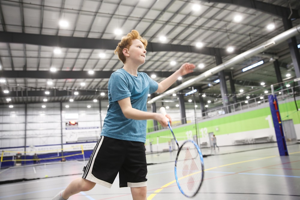 ragazzo in maglietta girocollo blu e pantaloncini neri che gioca a badminton al chiuso