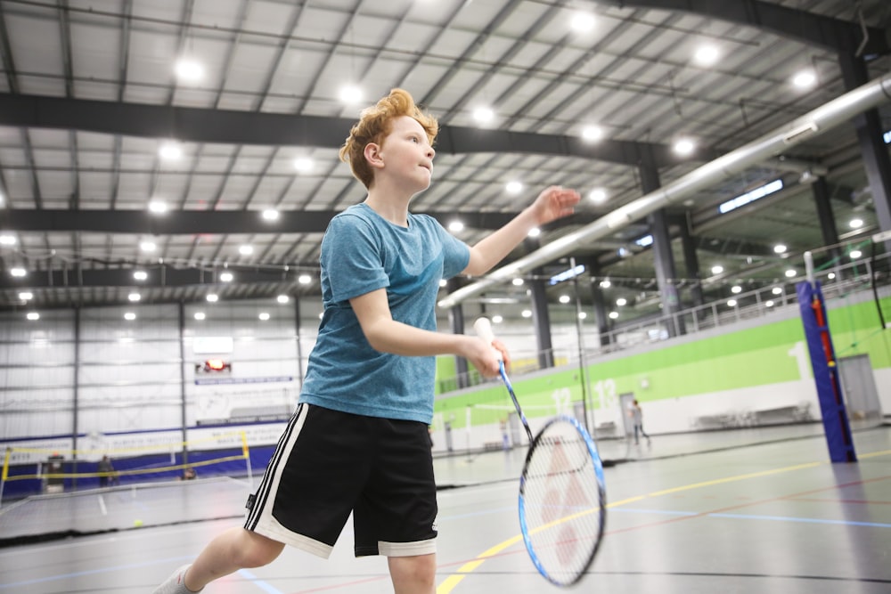 boy in blue crew-neck T-shirt and black shorts playing badminton indoors