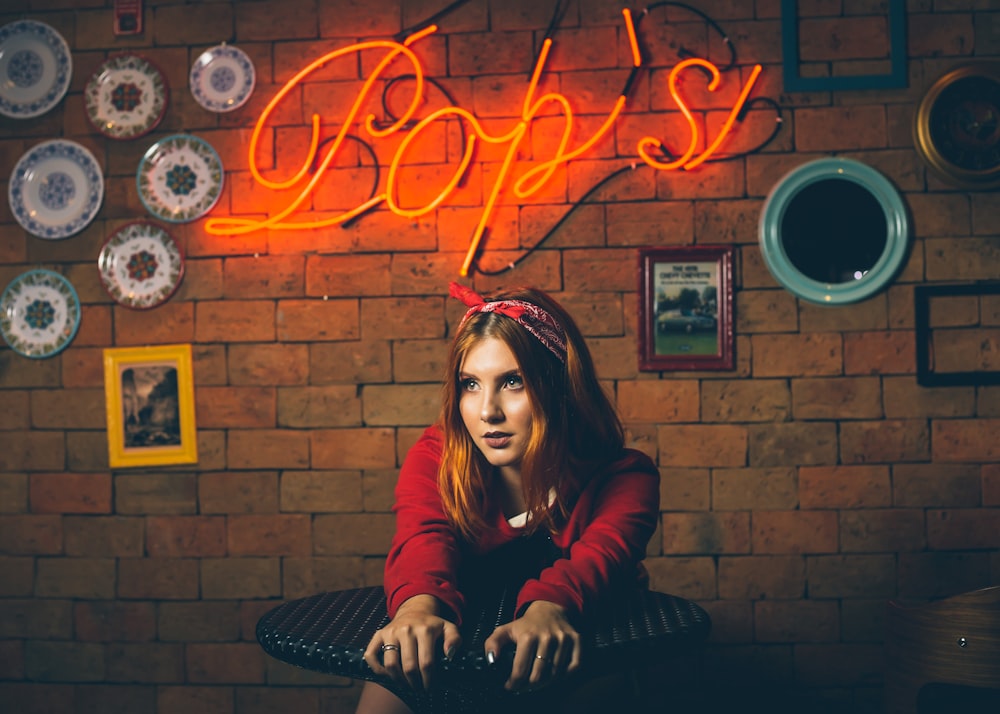 woman sitting beside table in front of Bop's neon sign