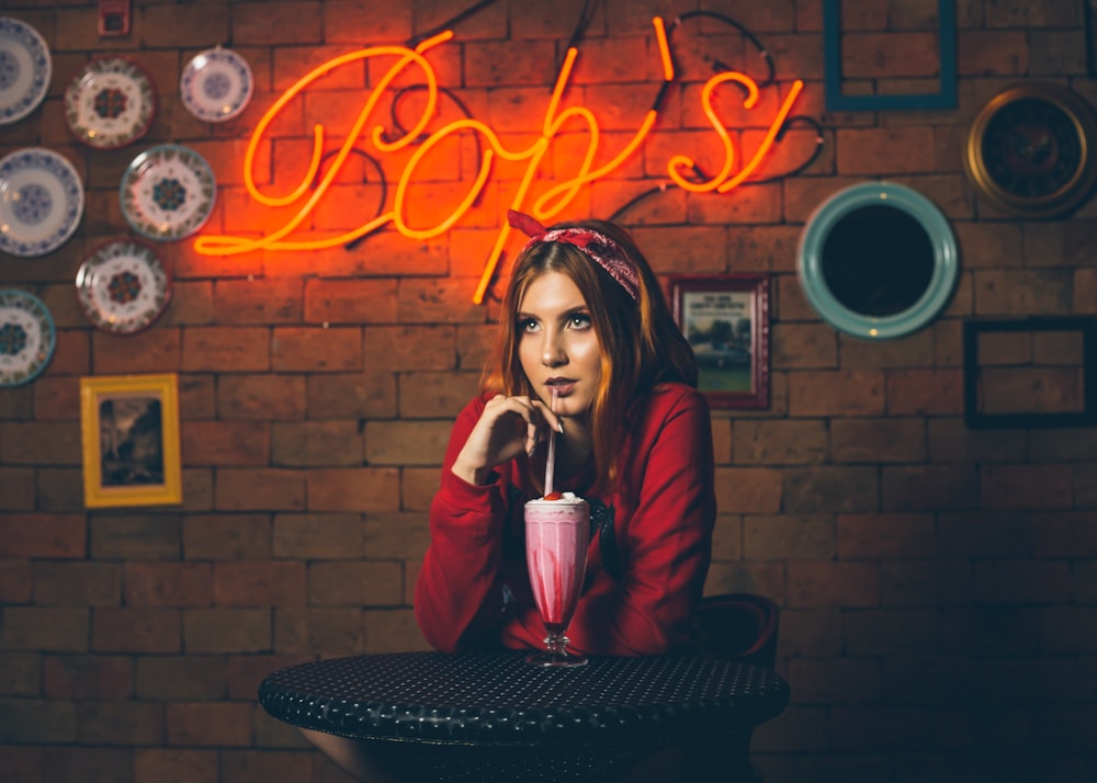 woman sipping drink sitting in front of Bop's neon sign