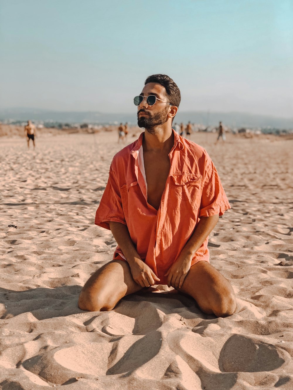 man in orange button-up shirt sitting on sand during daytime