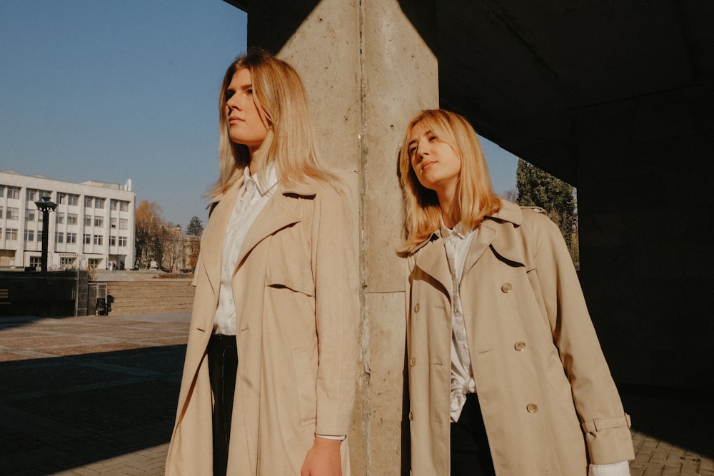two women wearing brown coat leaning on concrete pillar