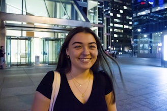 A young woman wearing a luartalme shirt with a shining half-moon under city lights.
