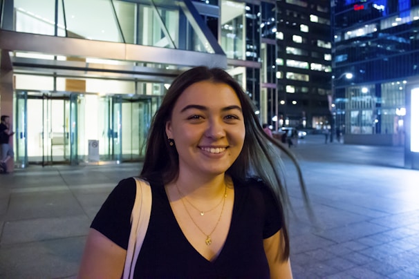 A young woman wearing a luartalme shirt with a shining half-moon under city lights.