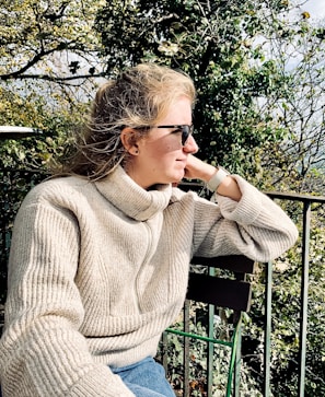 Casual chic outfit featuring a cozy knit sweater paired with sleek trousers on a sunlit balcony.