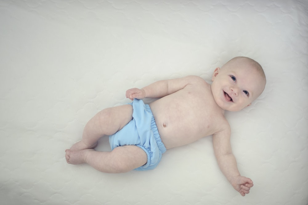bebé en pantalones azules acostado sobre una superficie blanca