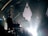 A band is performing on stage with instruments including a guitar, keyboard, and drums. The lighting is dim, creating a dramatic silhouette effect on the musicians. The background features geometric shapes and spotlights, with a haze from stage lighting.