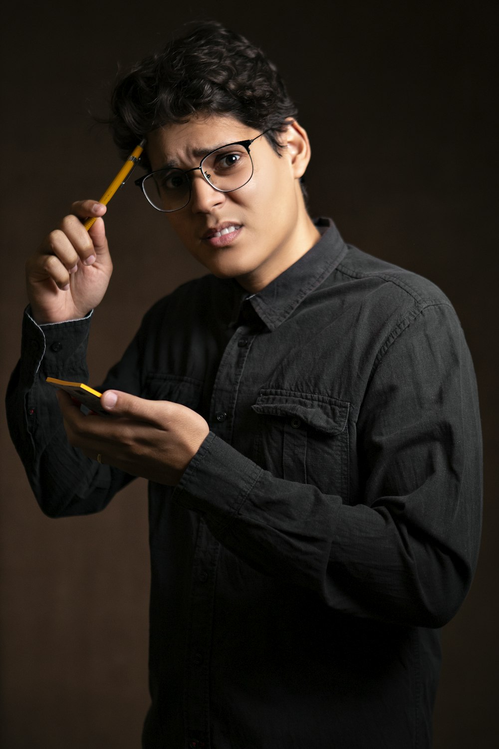黒のデニムジャケットを着た男性が鉛筆と黄色い付箋を持ち、困惑した様子で立っている