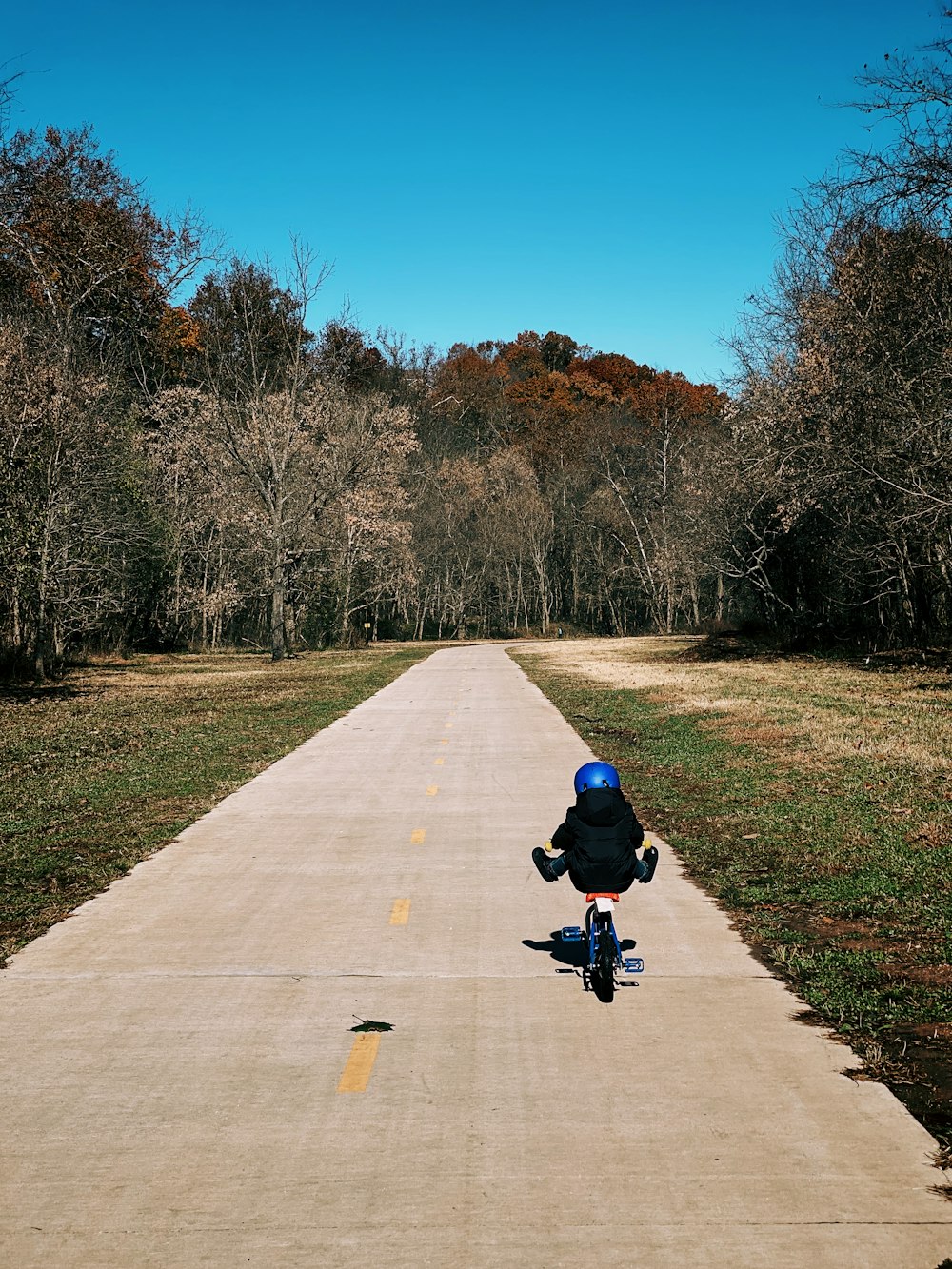 child biking on road near green field during daytime