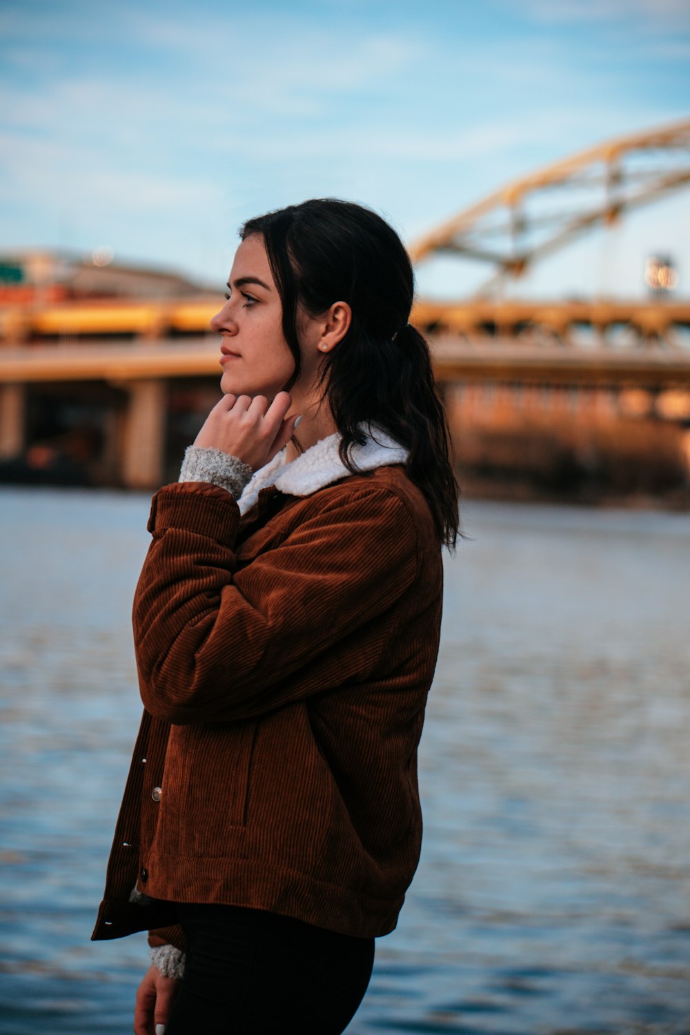 woman in brown jacket standing beside body of water