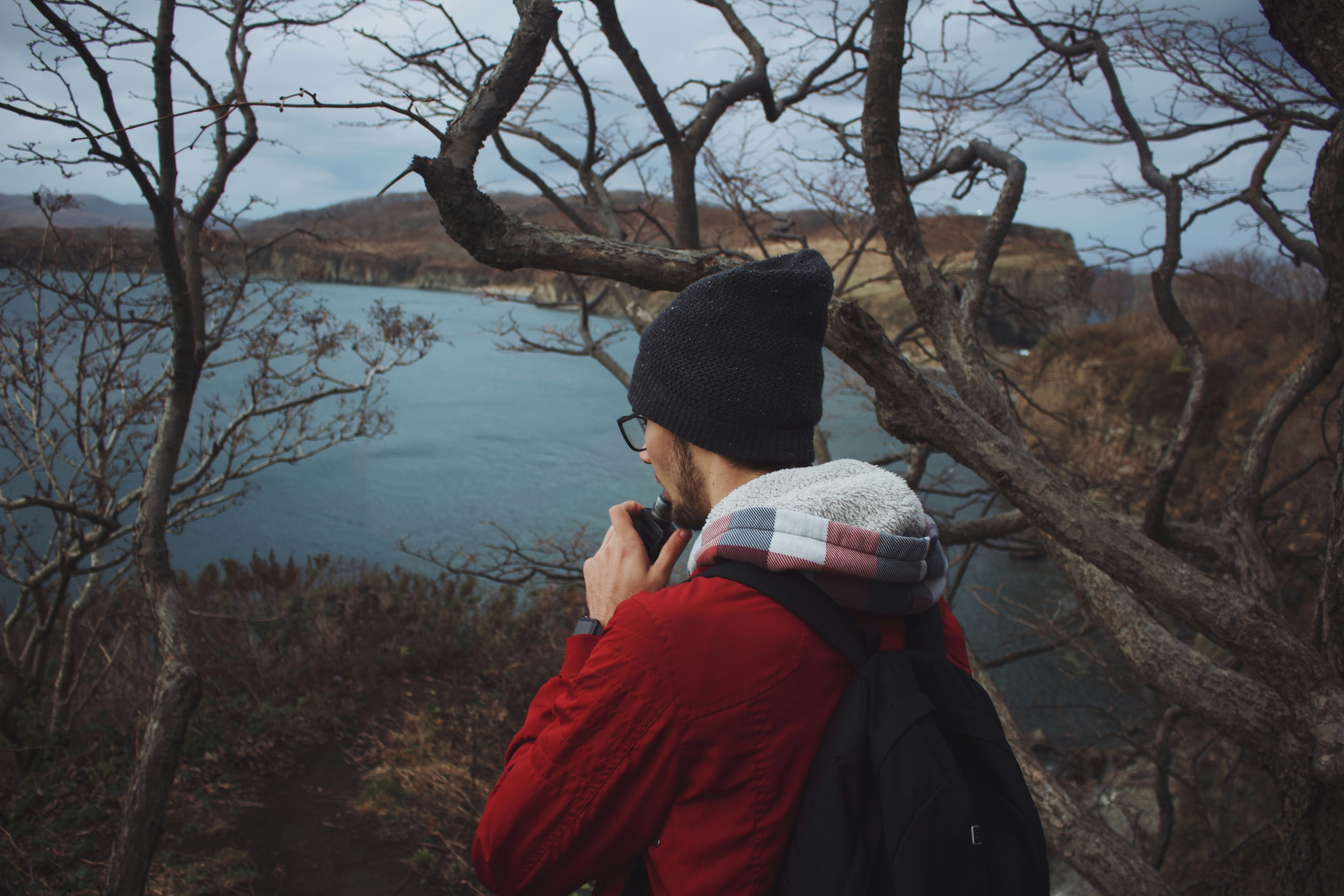 Una persona sentada en un sofá, mira tranquilamente por la ventana hacia un paisaje verde, con el smartphone boca abajo a su lado.