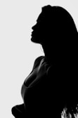 A female silhouette is shown in profile against a light background. The outline of her face, shoulder, and torso is visible, with long hair cascading down her back. The image is in black and white, highlighting the contours and curves of the figure.