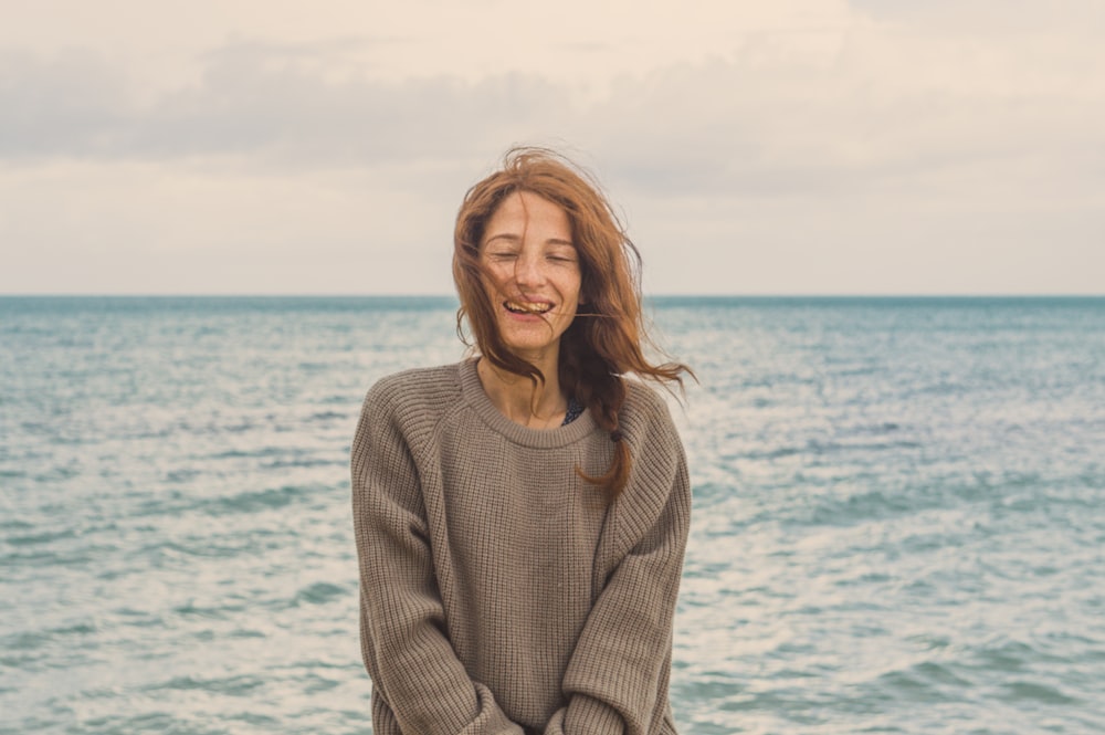 smiling woman wearing gray sweater on seashore