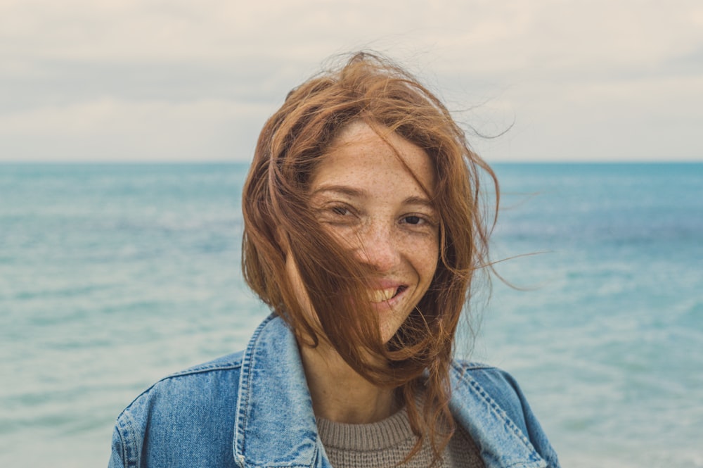 smiling woman in blue denim jacket behind sea