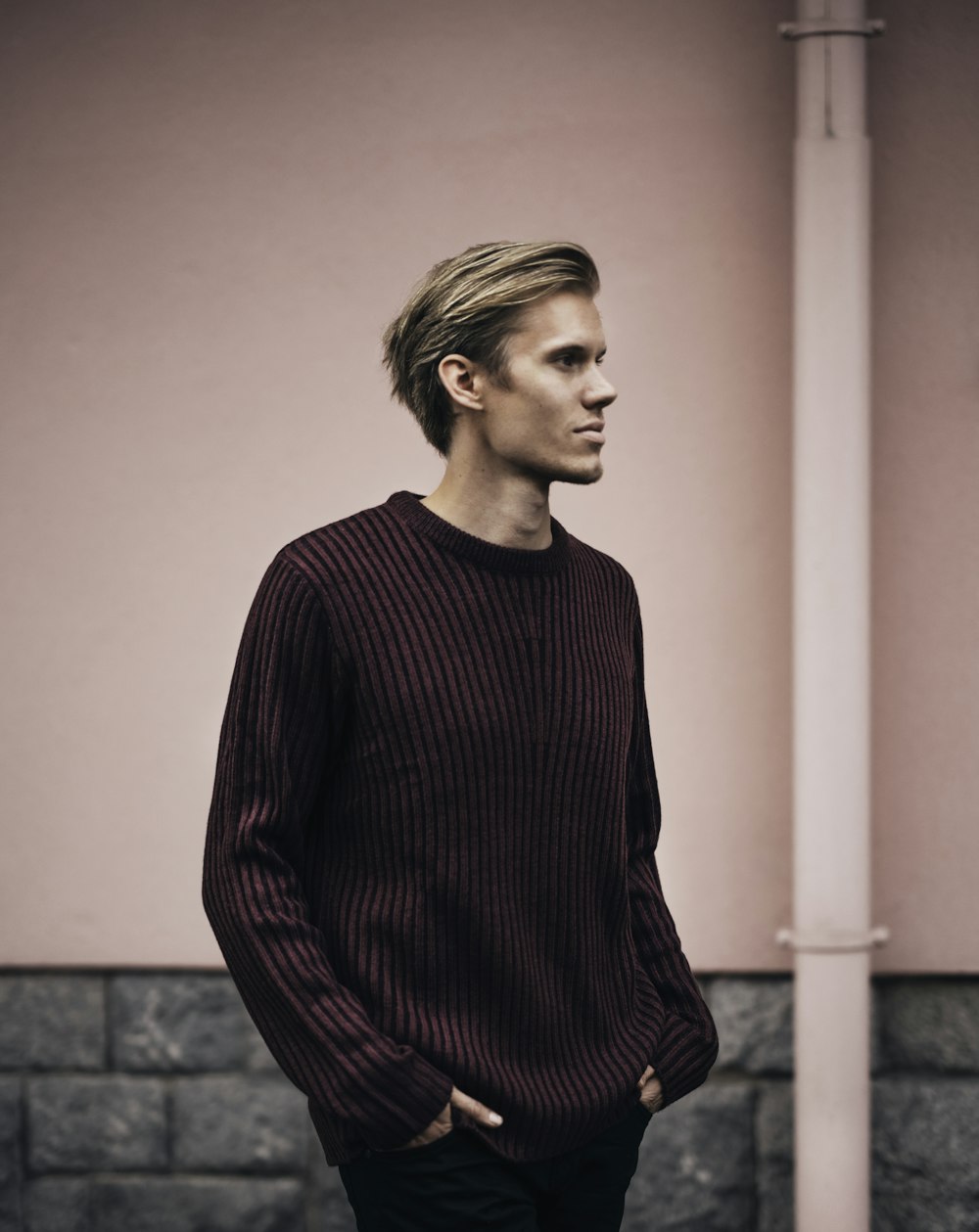 man in brown sweater standing beside wall