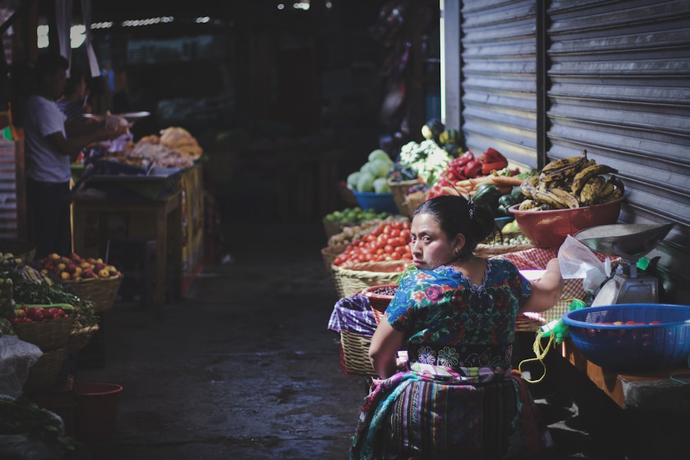 woman in floral top by displayed fruits and vegetables