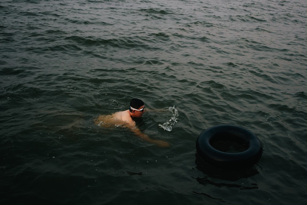 man swimming near black life ring