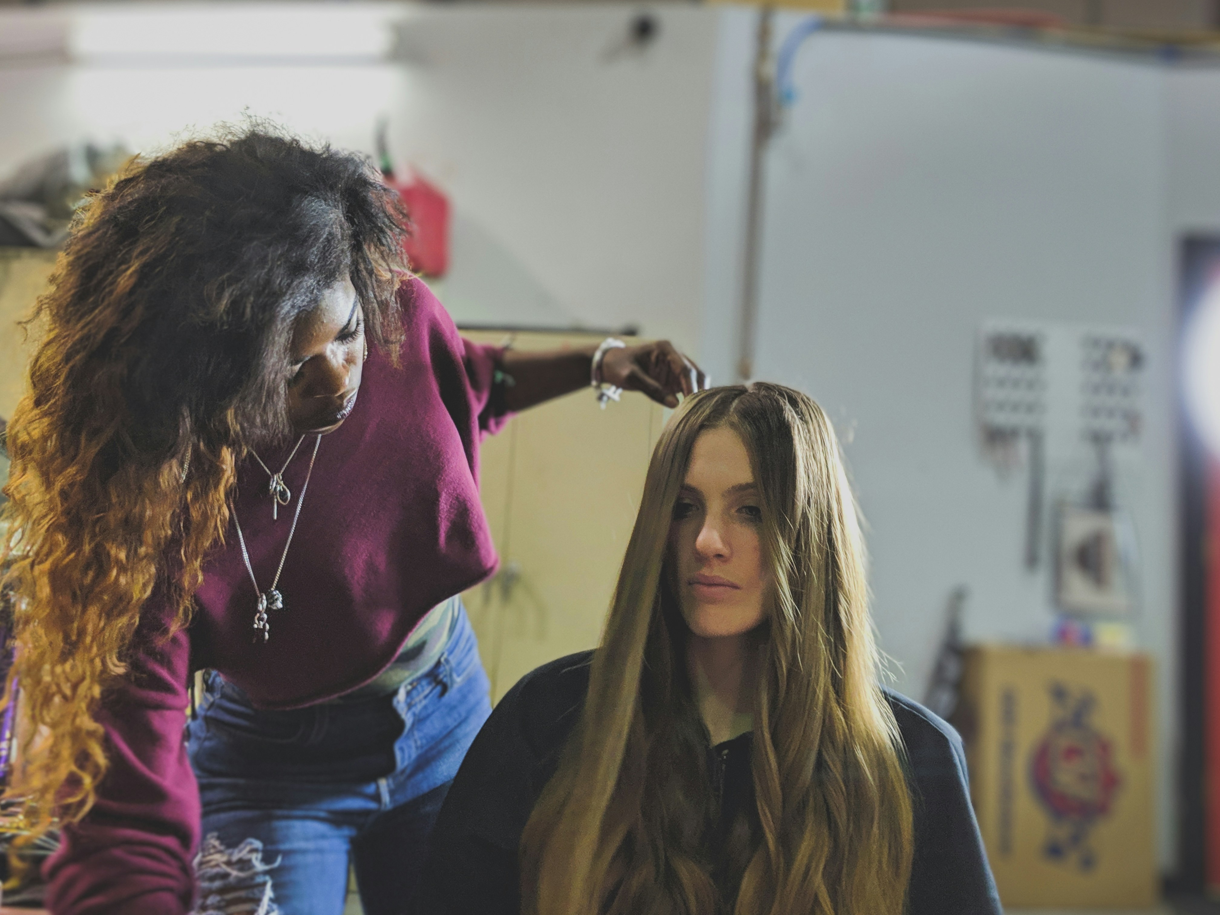 A stylist in a burgundy crop top works with her model before a shoot. Shot inside a repair shop located in Sterling Virginia.