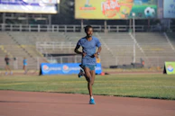 A male athlete sprinting on a track stadium under bright lights.