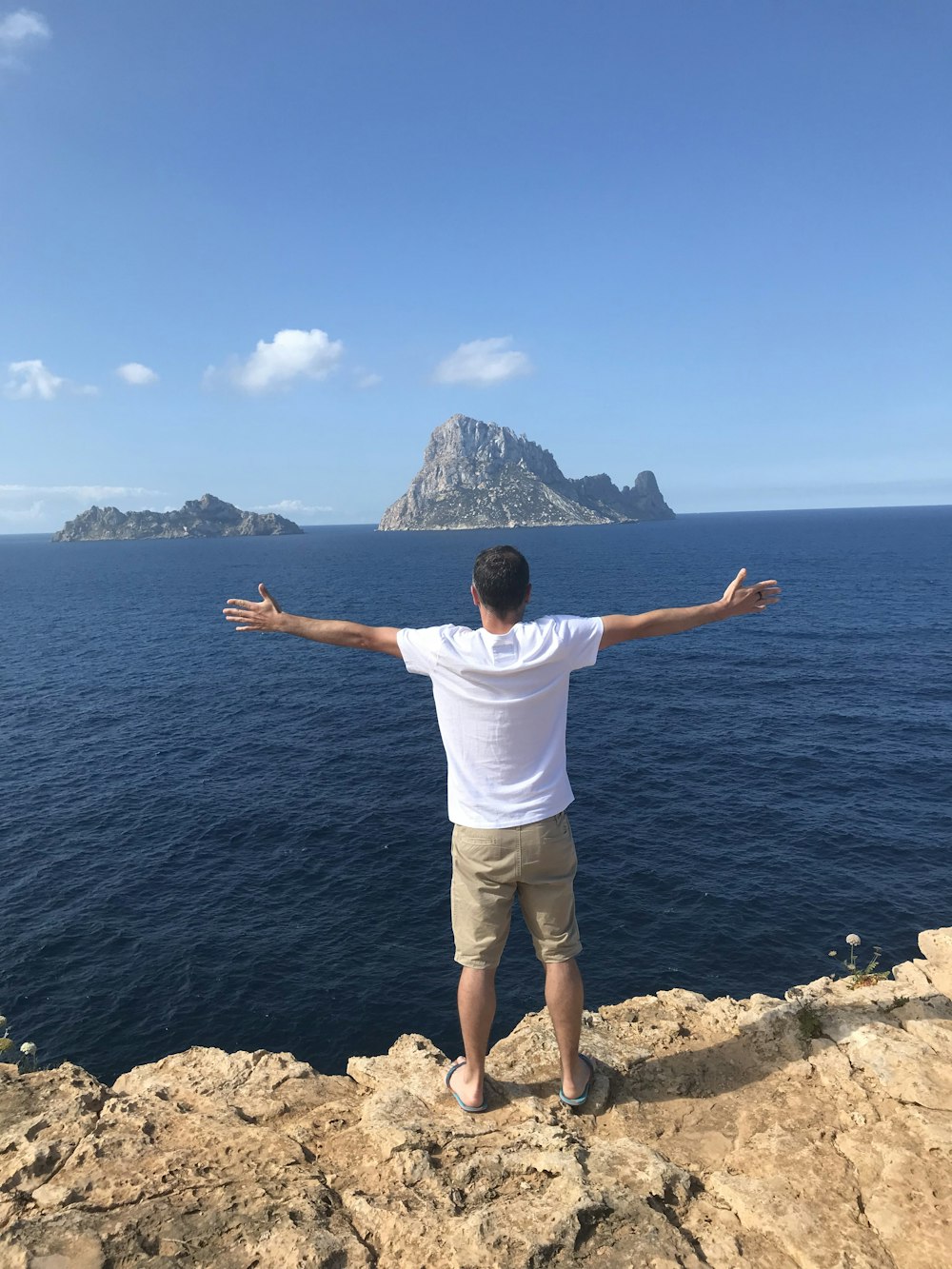 Hombre de pie en la isla rocosa extendiendo los brazos y mirando hacia el océano durante el día