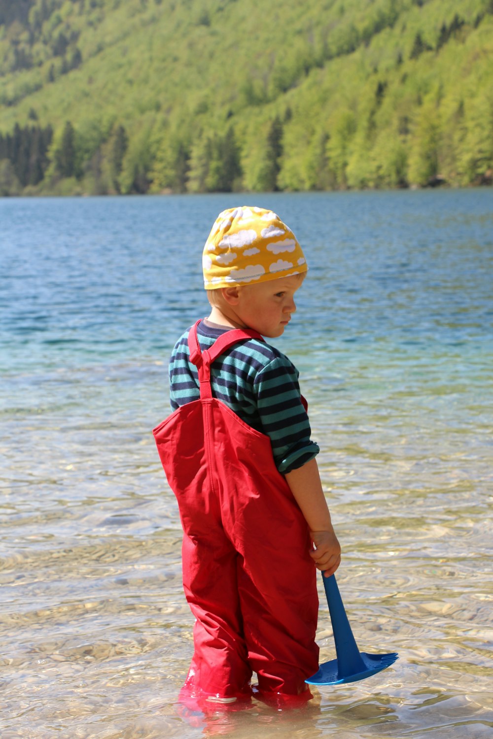 boy in red dungarees standing on seashore