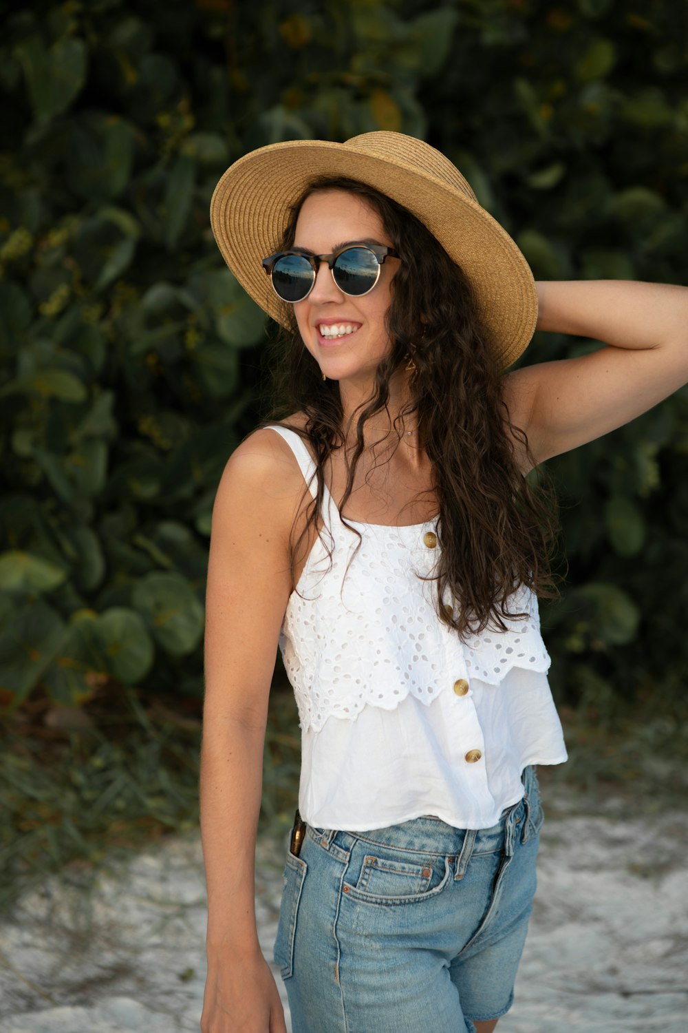 woman in white cami top and blue denim shorts standing near green plants