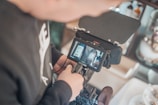 A person is operating a camera with a small monitor displaying two bottles. The setup appears to be in a professional environment focusing on product videography or photography.