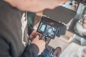 A person is operating a camera with a small monitor displaying two bottles. The setup appears to be in a professional environment focusing on product videography or photography.