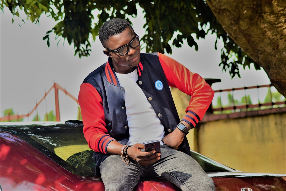 a man sitting on the hood of a car looking at his cell phone