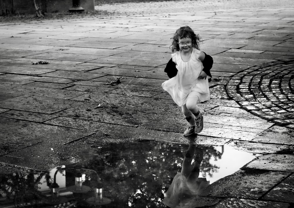 grayscale photography of girl about to run over water puddle