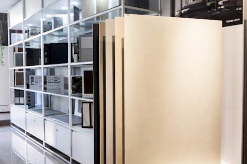 A display area in a showroom with vertical panels leaning against a shelving unit filled with color and material samples. The shelving is organized with various swatches and sample boards.