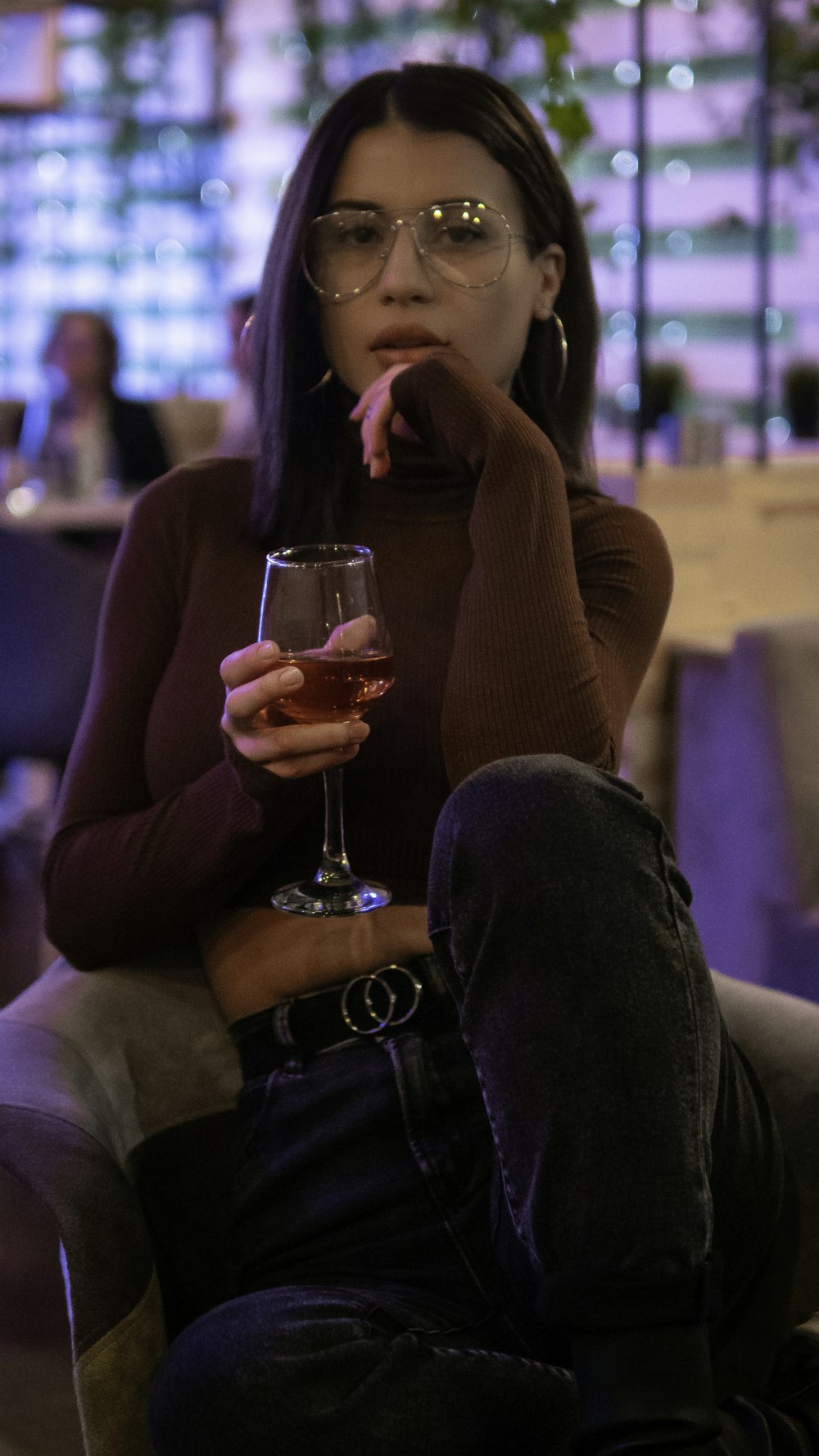 woman holding glass of wine sitting on chair while putting left hand near her chin