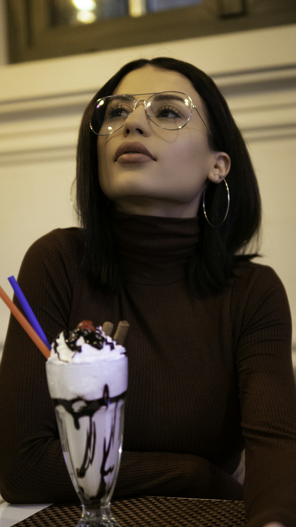 woman wearing brown turtleneck long-sleeved blouse sitting near table and chocolate drink on table