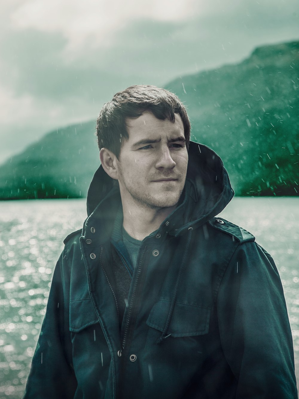 man wearing black zip-up jacket standing near body of water in rainy day