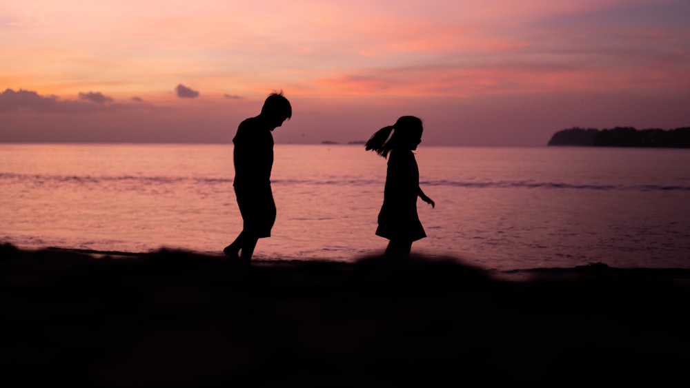 silhouette photography of boy and girl walking beside shoreline