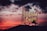 A neon sign featuring the words 'Portland Oregon' with 'Old Town' below, illuminated against a dramatic sunset sky. The sign is topped by a white stag silhouette, and the sky is a vibrant blend of red, orange, and dark clouds.