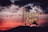 A neon sign featuring the words 'Portland Oregon' with 'Old Town' below, illuminated against a dramatic sunset sky. The sign is topped by a white stag silhouette, and the sky is a vibrant blend of red, orange, and dark clouds.