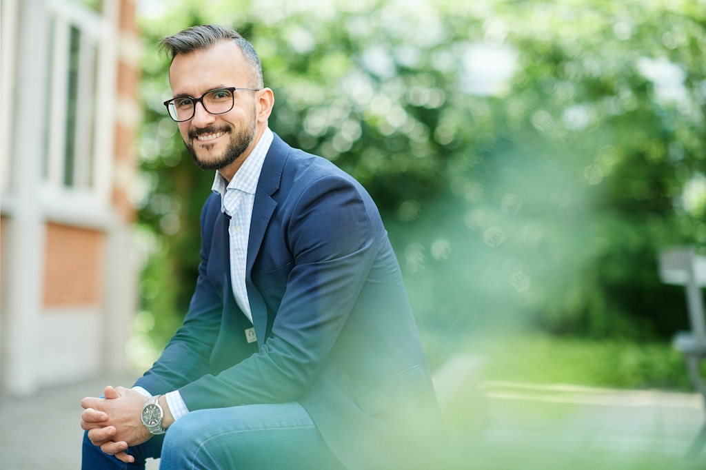 man wearing blue formal suit and eyeglasses sitting and smiling