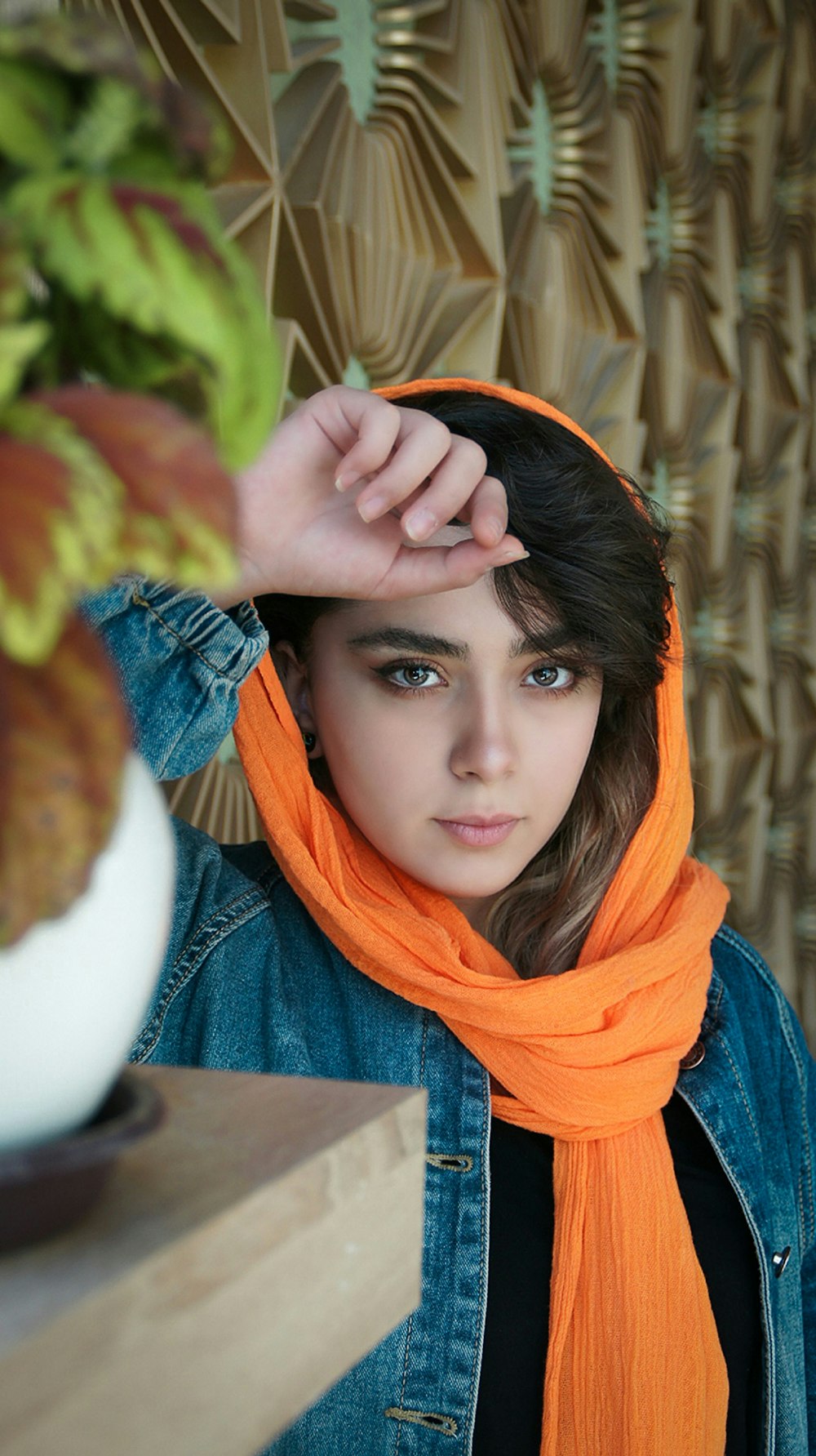 woman wearing blue denim button-up jacket and orange scarf standing and leaning near brown wooden plank