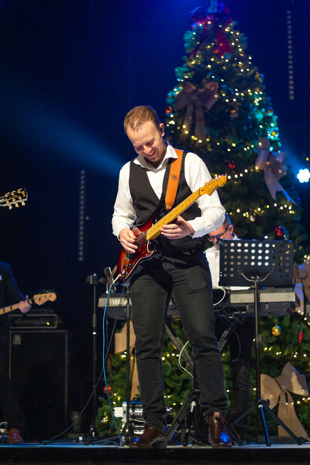 man playing red and brown guitar beside Christmas tree