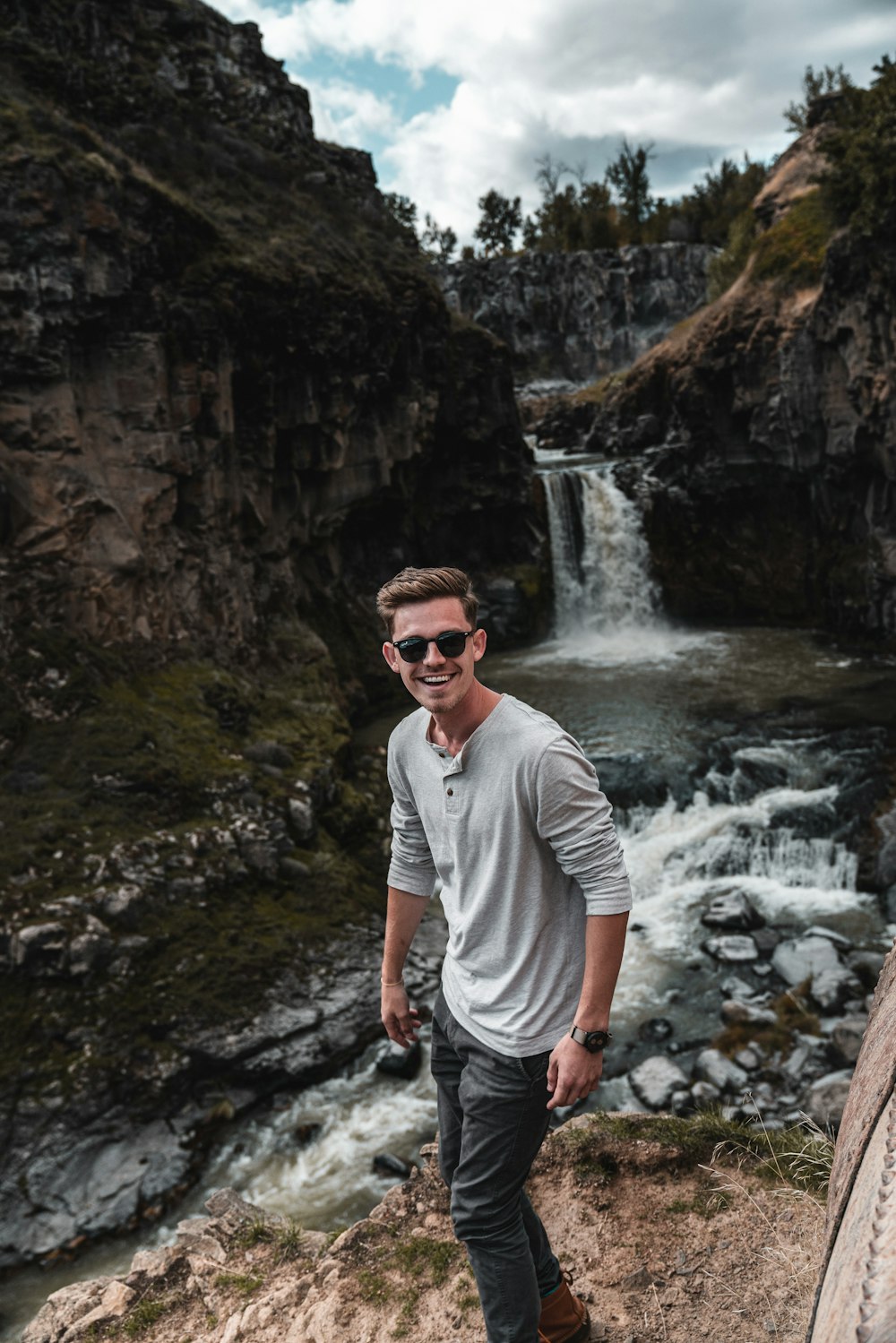 man standing on stone cliff near waterfalls during daytime