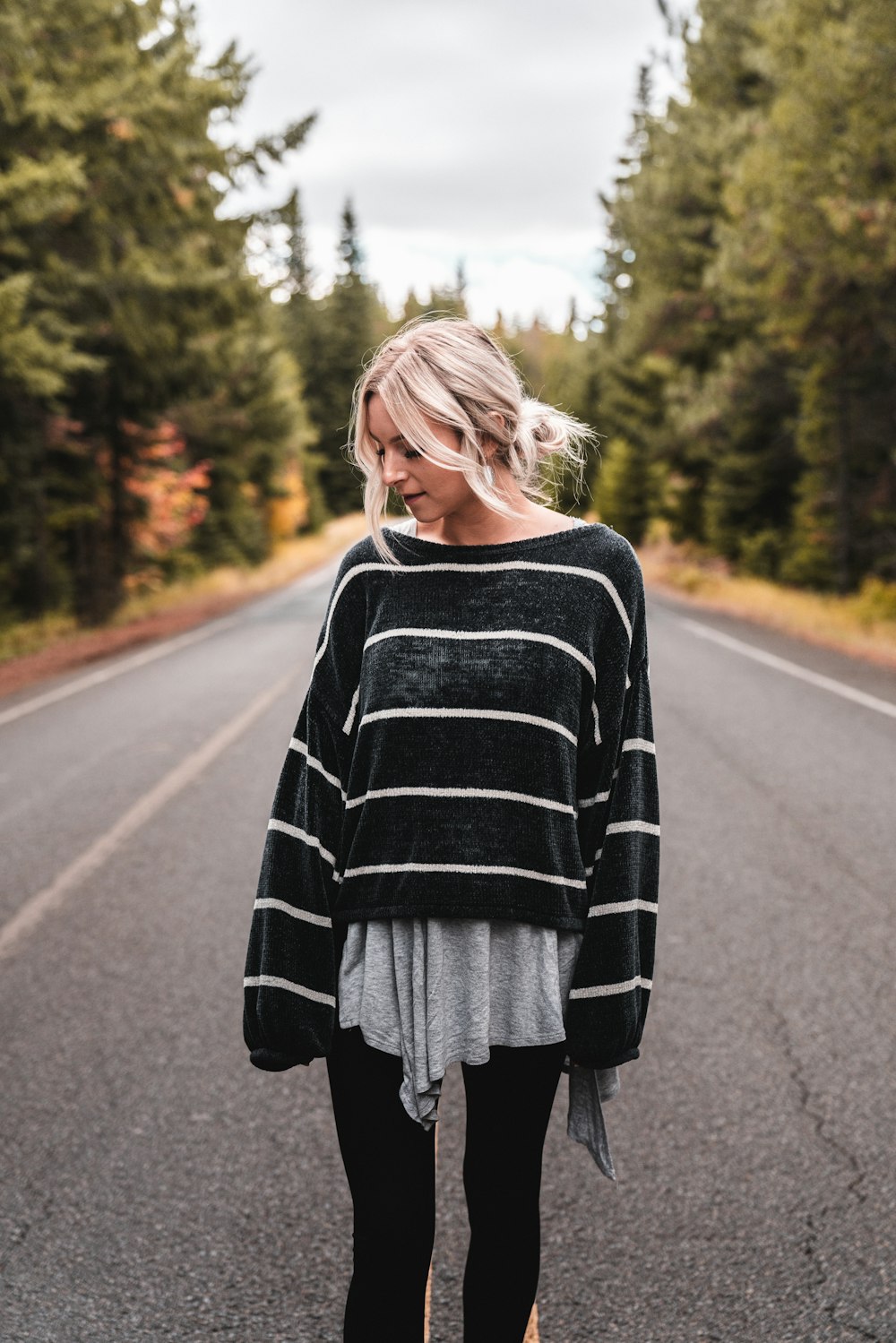 woman wearing black and white striped long-sleeved jacket while standing on road during daytime