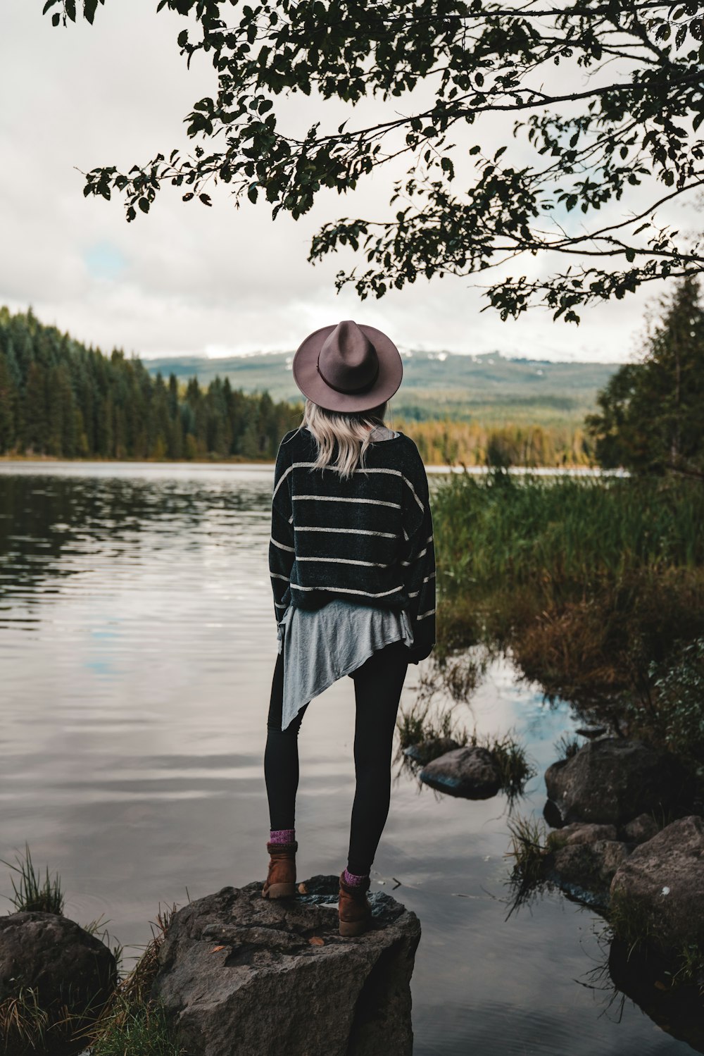 woman standing on stone near lake and trees during daytime