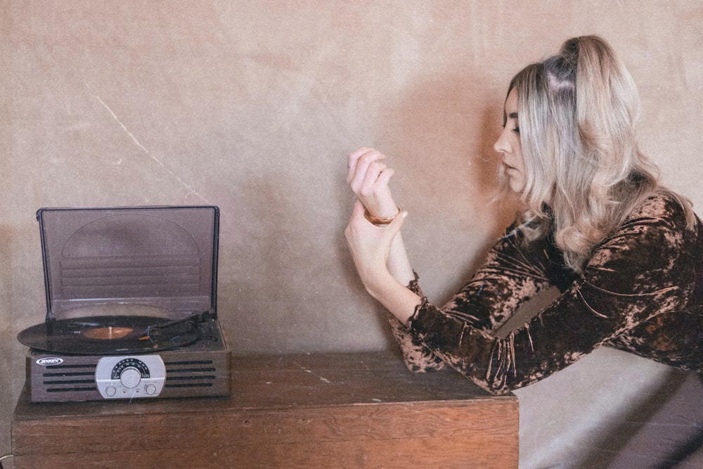 woman in brown long-sleeved shirt sitting by the table with vinyl player on top