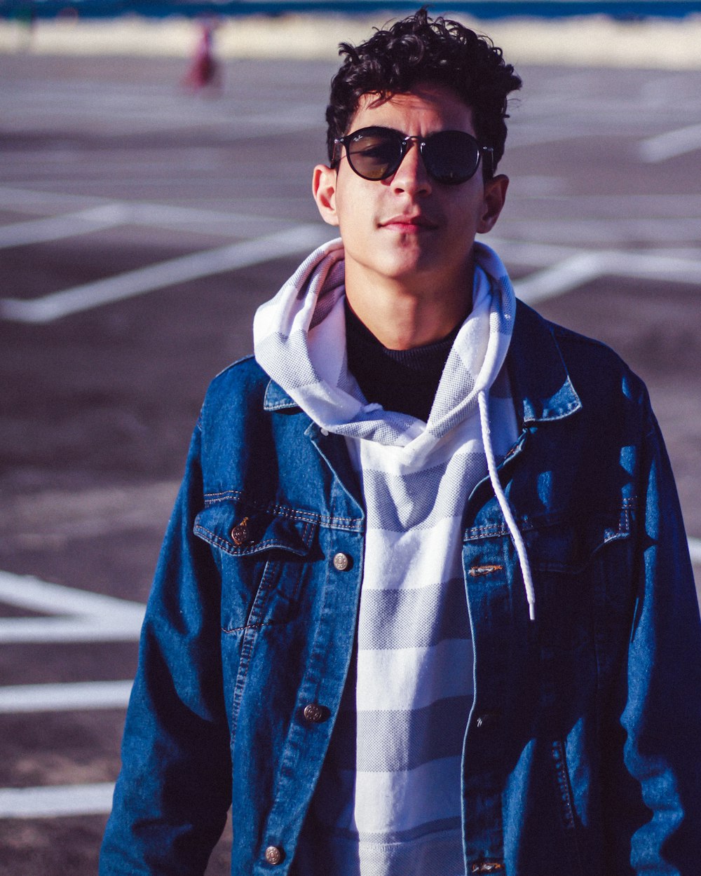 man wearing blue button-up denim jacket and sunglasses standing and smiling